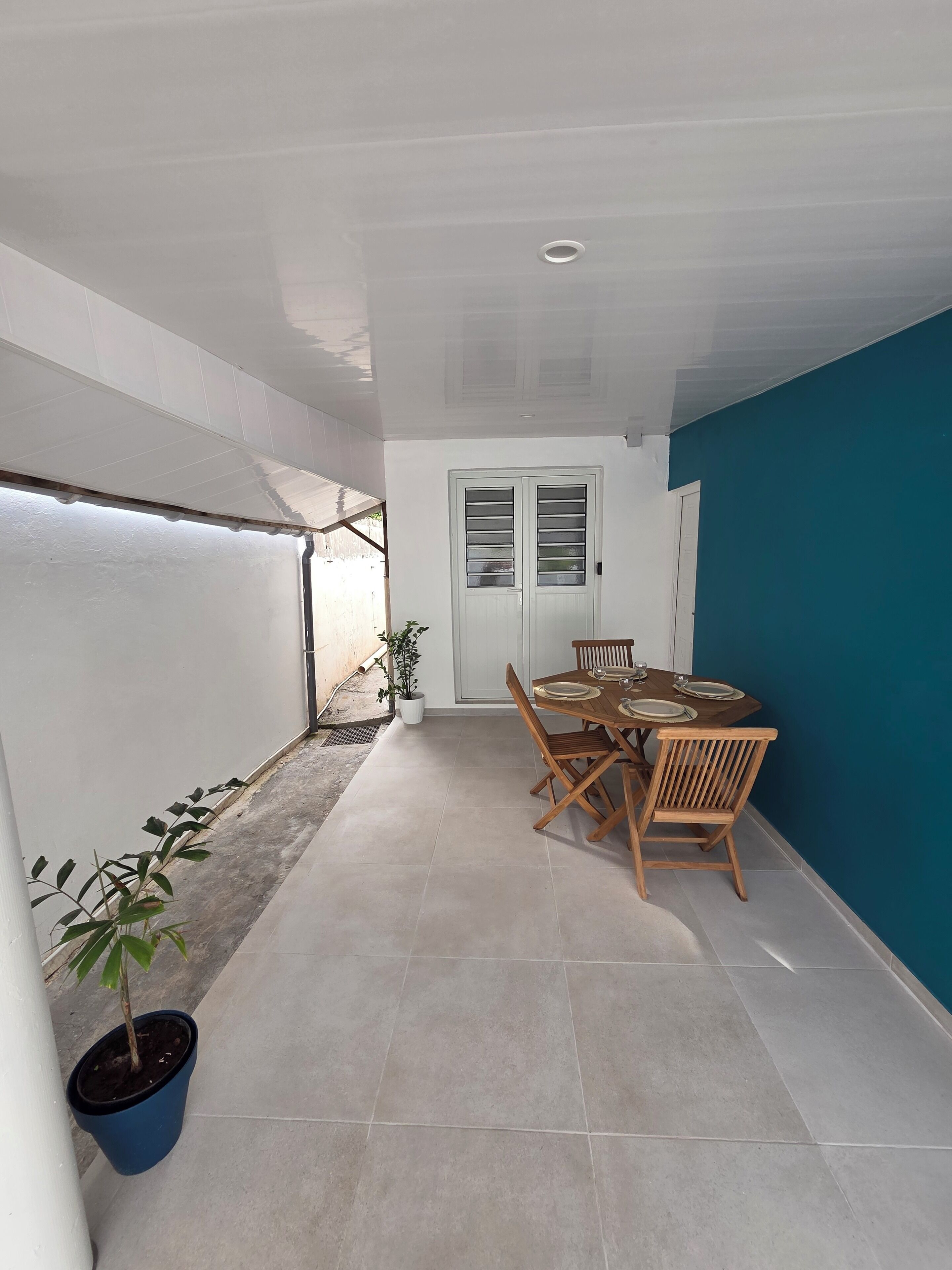 Um quarto com uma mesa de jantar posta para quatro pessoas, uma planta em vaso e uma porta com janela.