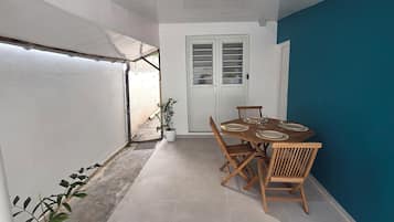 Um quarto com uma mesa de jantar posta para quatro pessoas, uma planta em vaso e uma porta com janela.