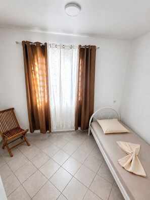 A small, single-bed room with a wooden chair and a window with brown curtains.