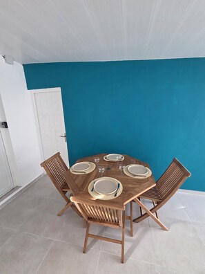 A round wooden table with four chairs, set for dining, against a blue wall with a white door in the background.