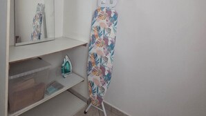 Ein Zimmer mit Kleiderschrank, Spiegel, Ablagefläche mit einer Plastikbox und Bügelbrett.