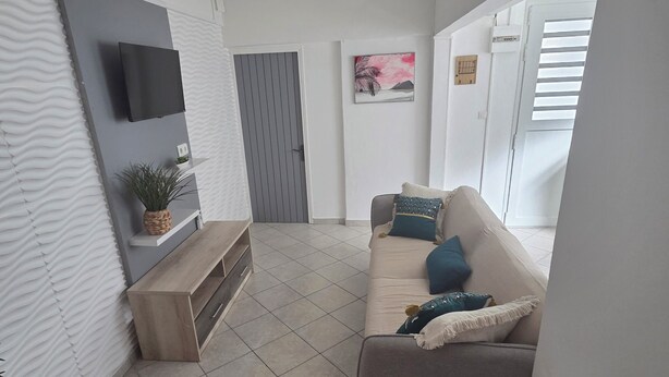 Ein modernes Wohnzimmer mit Flachbildfernseher, Deckenventilator, einer Couch mit Kissen, einer Holzbank und einem Topf mit Pflanze.