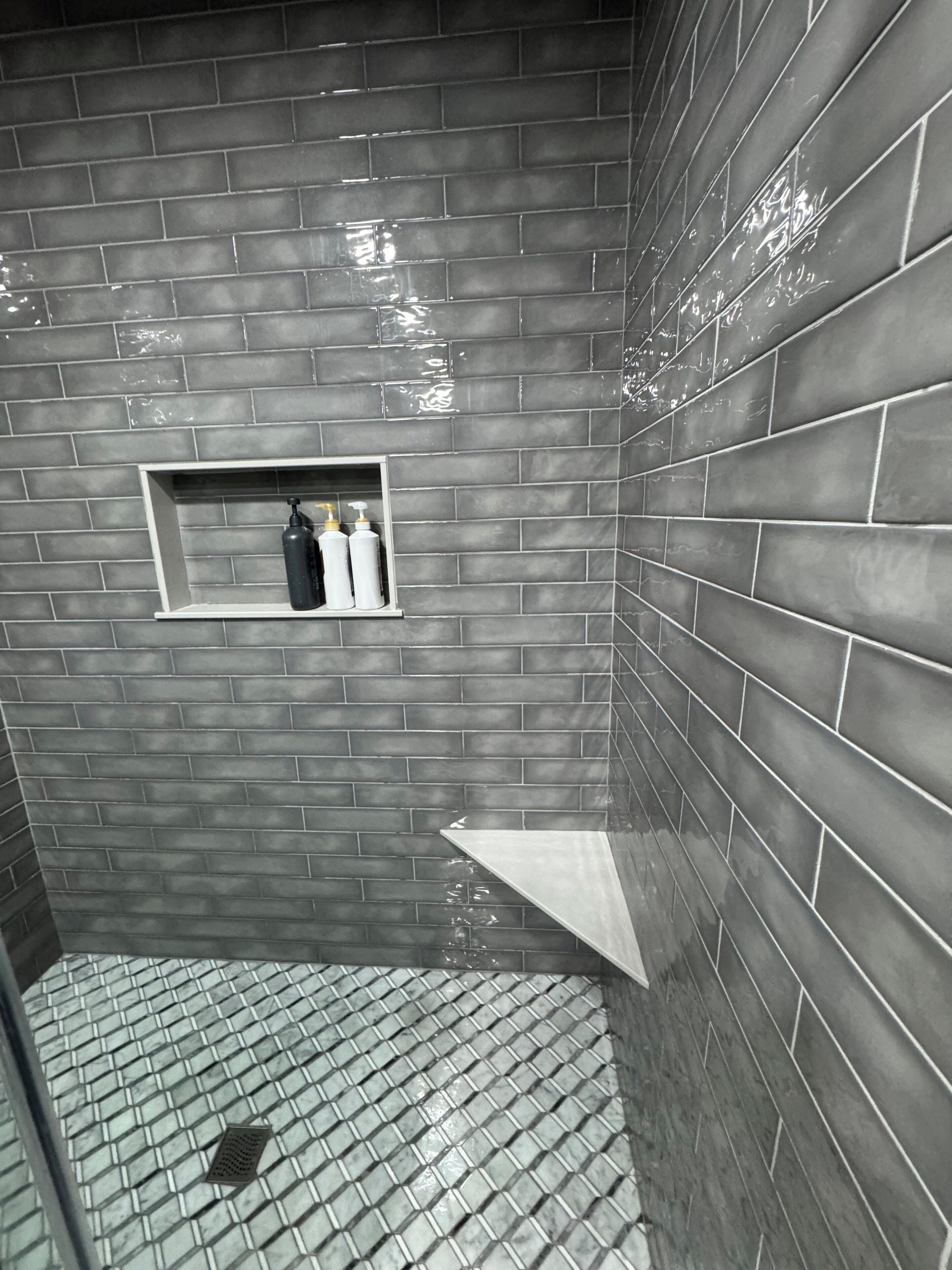 Une salle de bain avec un sol et des murs carrelés, une étagère contenant des articles de toilette et un espace douche.