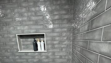 Une salle de bain avec un sol et des murs carrelés, une étagère contenant des articles de toilette et un espace douche.