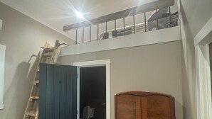 Ein Zimmer mit Deckenventilator, einer Holzleiter, einem Kleiderschrank und einer Tür zu einem dunklen Bereich.