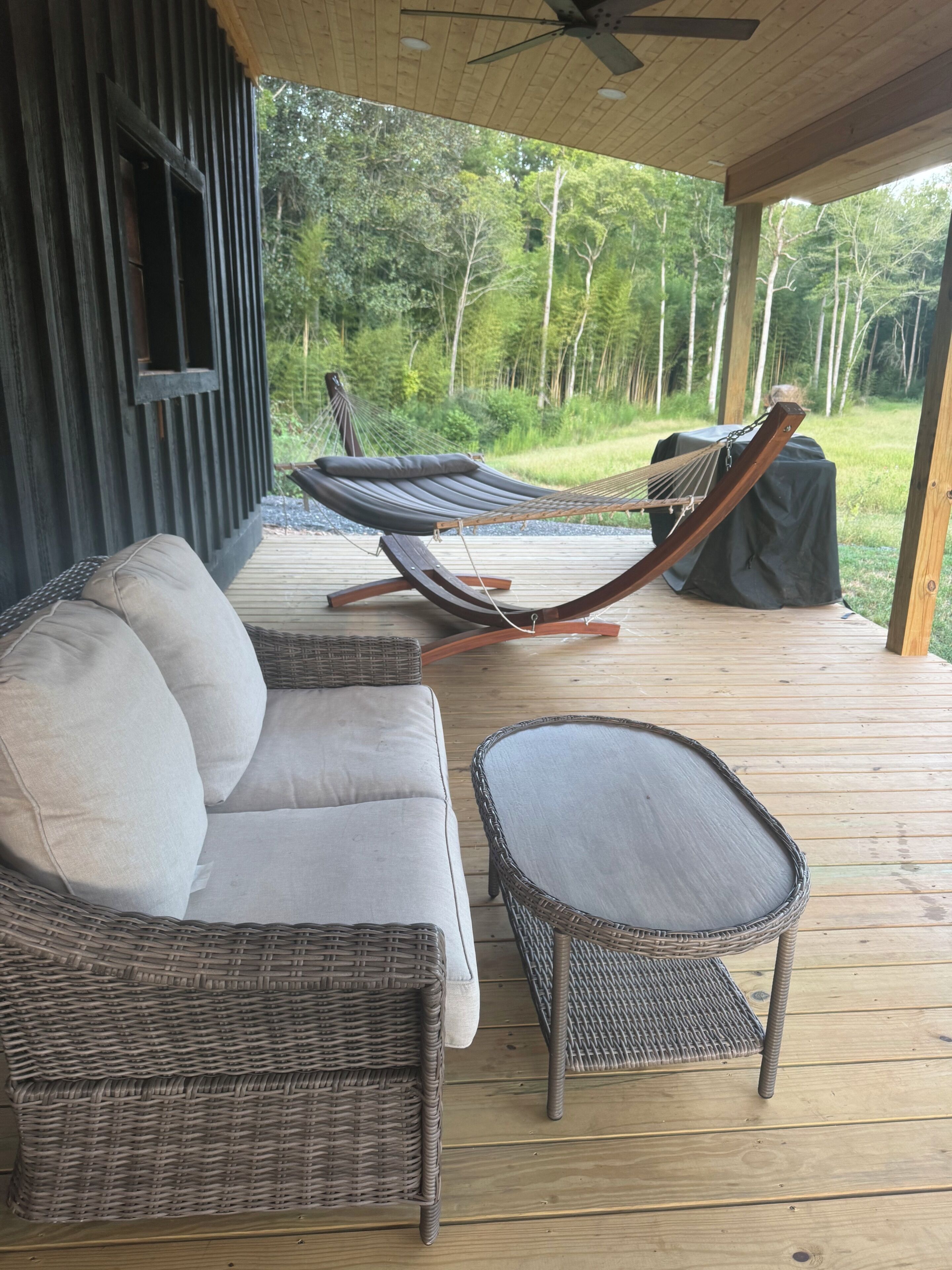 Un espace extérieur aménagé avec des meubles en osier, un hamac et une vue sur une zone boisée.