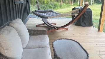 Un espace extérieur aménagé avec des meubles en osier, un hamac et une vue sur une zone boisée.