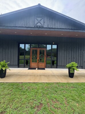 A building with a large wooden door, two potted plants, and a grassy area in front.