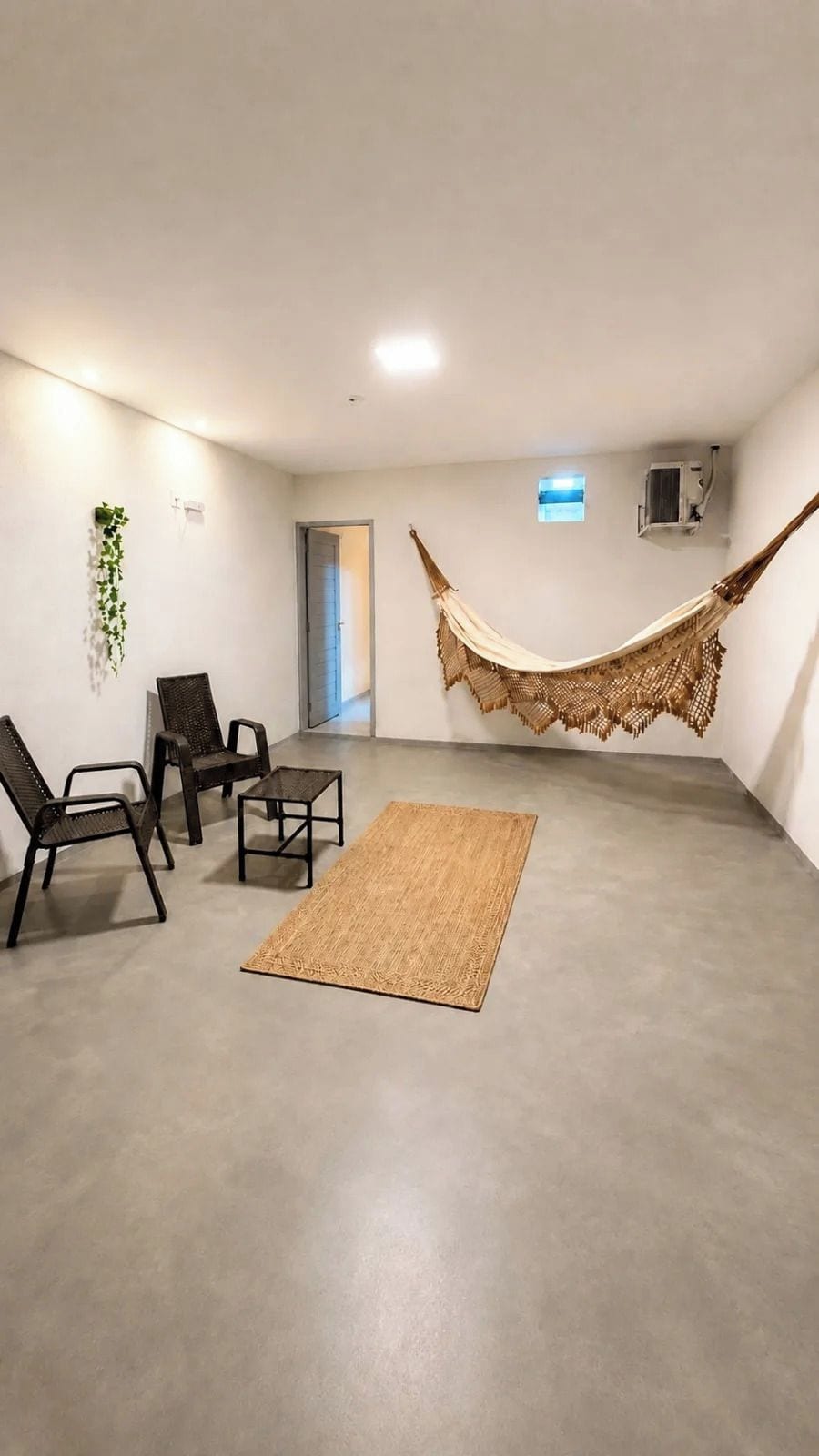 Una habitación con una hamaca, dos sillas, una mesita y una alfombra tejida.