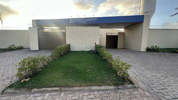 Entrada de hotel com um caminho de entrada pavimentado, gramado bem cuidado e uma placa azul para o River Campos Hotel.