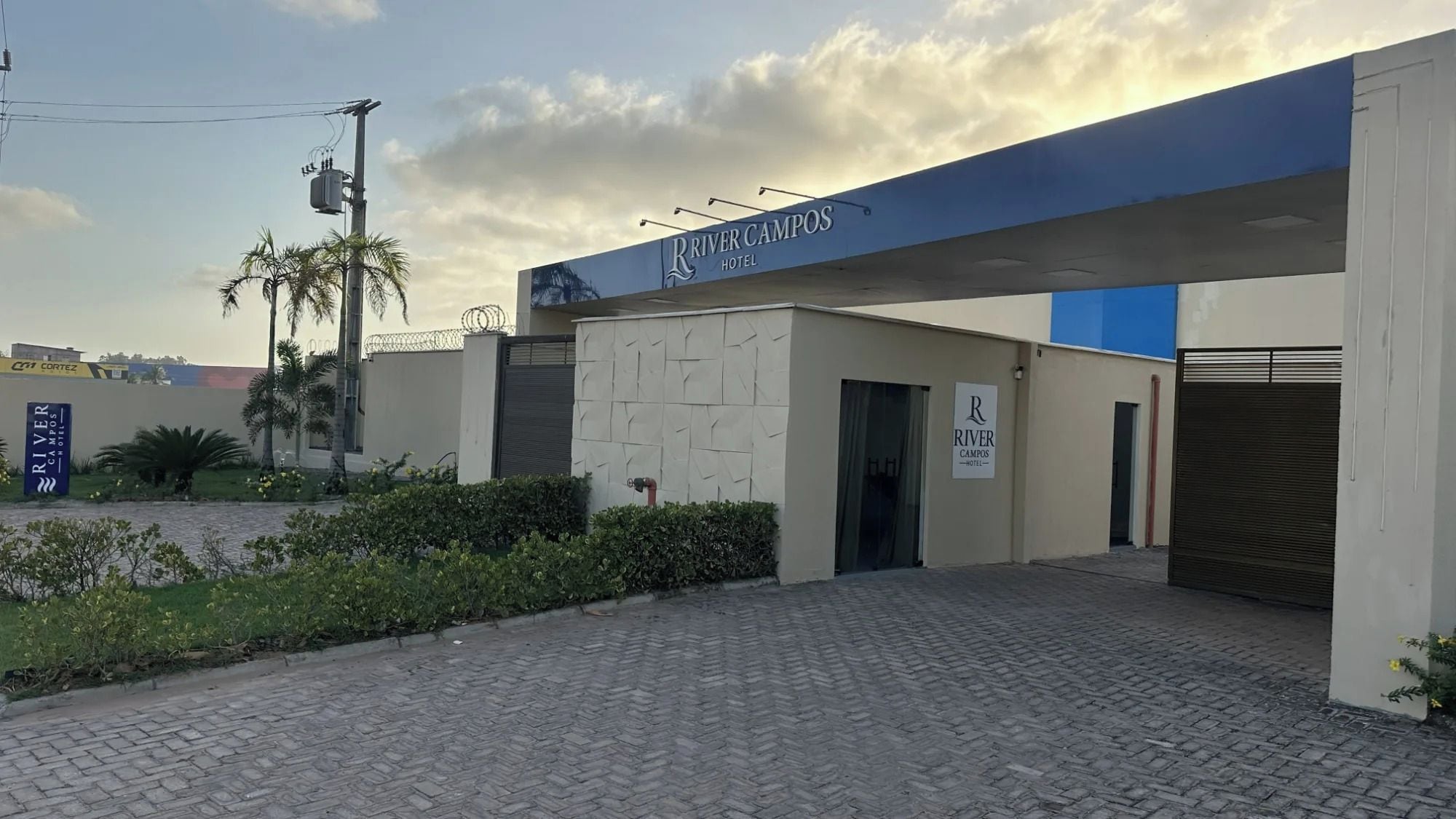 Exterior del Hotel River Campos con entrada pavimentada, un camino de acceso con puerta y cielo despejado.