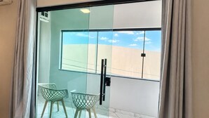 A room with a sliding glass door, two green chairs, a white wall, and a view of the sky.