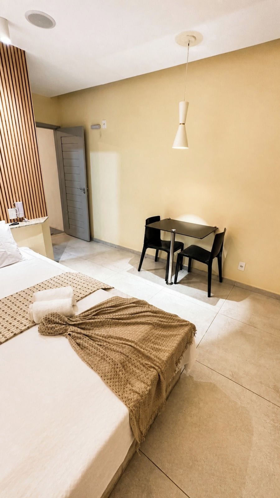 Una habitación de hotel con una cama, una mesa con sillas, una lámpara colgante y una puerta.