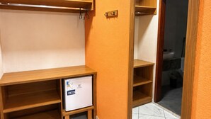 A room with a wooden desk, a small refrigerator, and a wardrobe with a mirror.