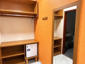 Una habitación con un escritorio de madera, un refrigerador pequeño y un armario con espejo.