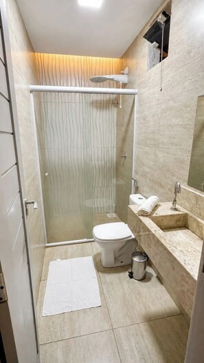 Un baño moderno con cabina de ducha de vidrio, inodoro, lavabo y espejo.