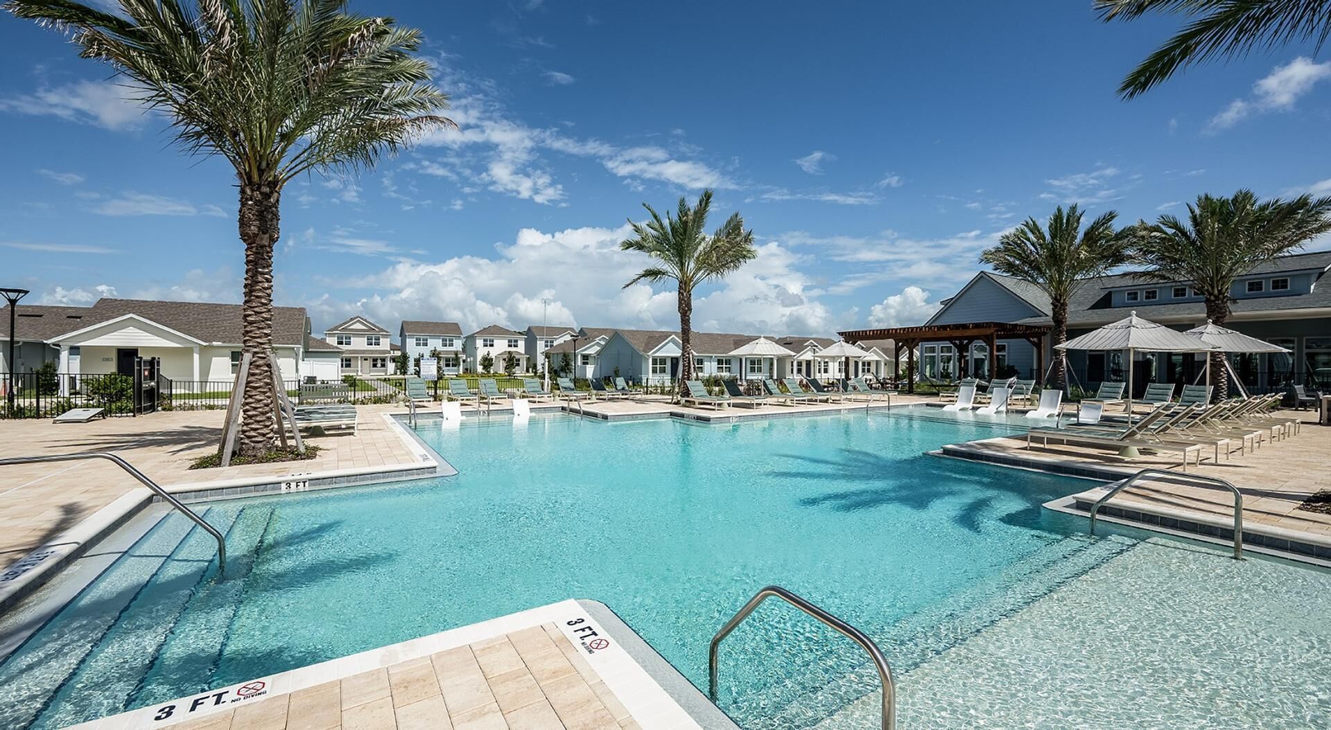 A swimming pool with lounge chairs and palm trees, surrounded by buildings.