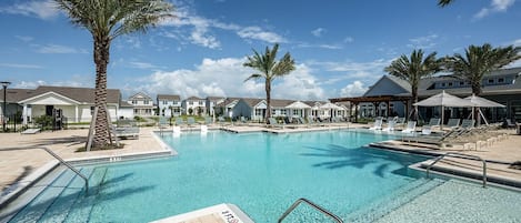 A swimming pool with lounge chairs and palm trees, surrounded by buildings.