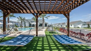 A covered outdoor area with a pool, two hammock chairs, and a view of residential buildings. - Landing | Amazing 2BD, Gym, Yoga Studio (Four Corners)