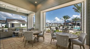 Ein überdachter Patio-Bereich mit Korbmöbeln und Blick auf einen Pool sowie Resort-Gebäude.