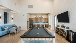 A modern living room with a pool table, a blue sofa, and a kitchen area in the background. - Landing | Amazing 2BD, Gym, Yoga Studio (Four Corners)
