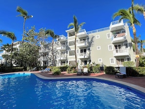 A hotel with a swimming pool, palm trees, and multiple balconies. - CARIBBEAN STUDIOS playa LOS CORALES (Punta Cana)