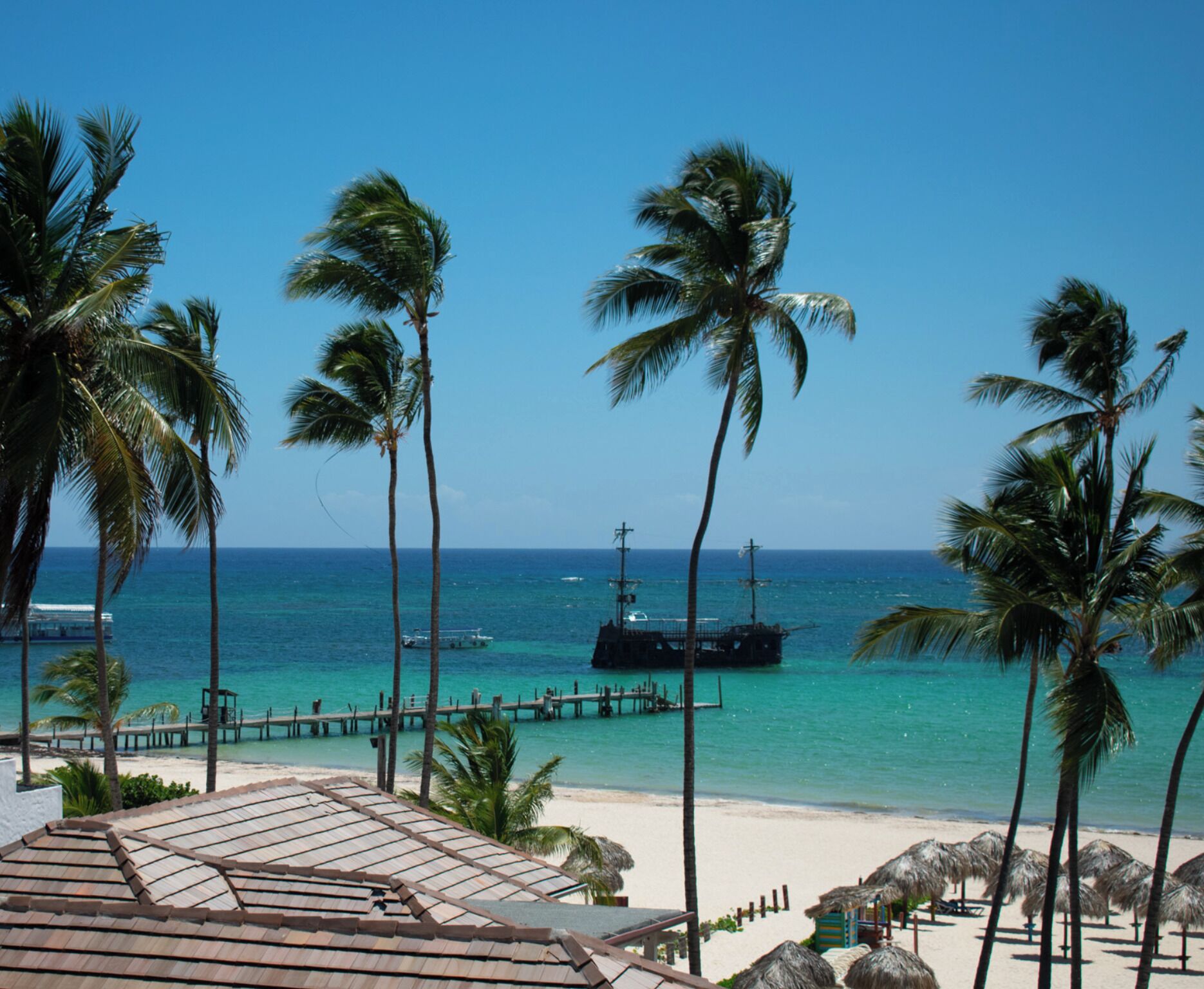 A beach view with palm trees, a pier, and a boat in the water.