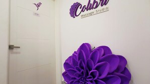 Un pasillo con una gran decoración floral púrpura, una puerta con la etiqueta '218' y un cartel en la pared que dice 'Colibri Studio Message Studio'.
