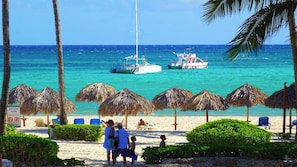 A beach with thatched umbrellas, a sandy shore, and boats in the water. - CARIBBEAN STUDIOS playa LOS CORALES (Punta Cana)