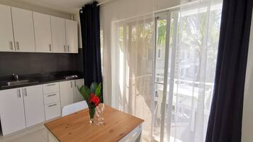 Una cocina moderna con armarios blancos y una encimera negra, una mesa de madera con un jarrón de flores rojas y un ventanal corredero que da a un área exterior.