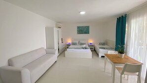 Un dormitorio moderno y bien iluminado con una cama grande, mesitas de noche, un sofá, una mesa de madera y una silla.