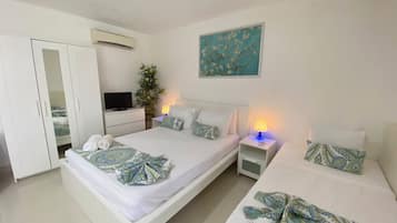 A hotel room with two beds, a TV, a plant, and a painting on the wall.
