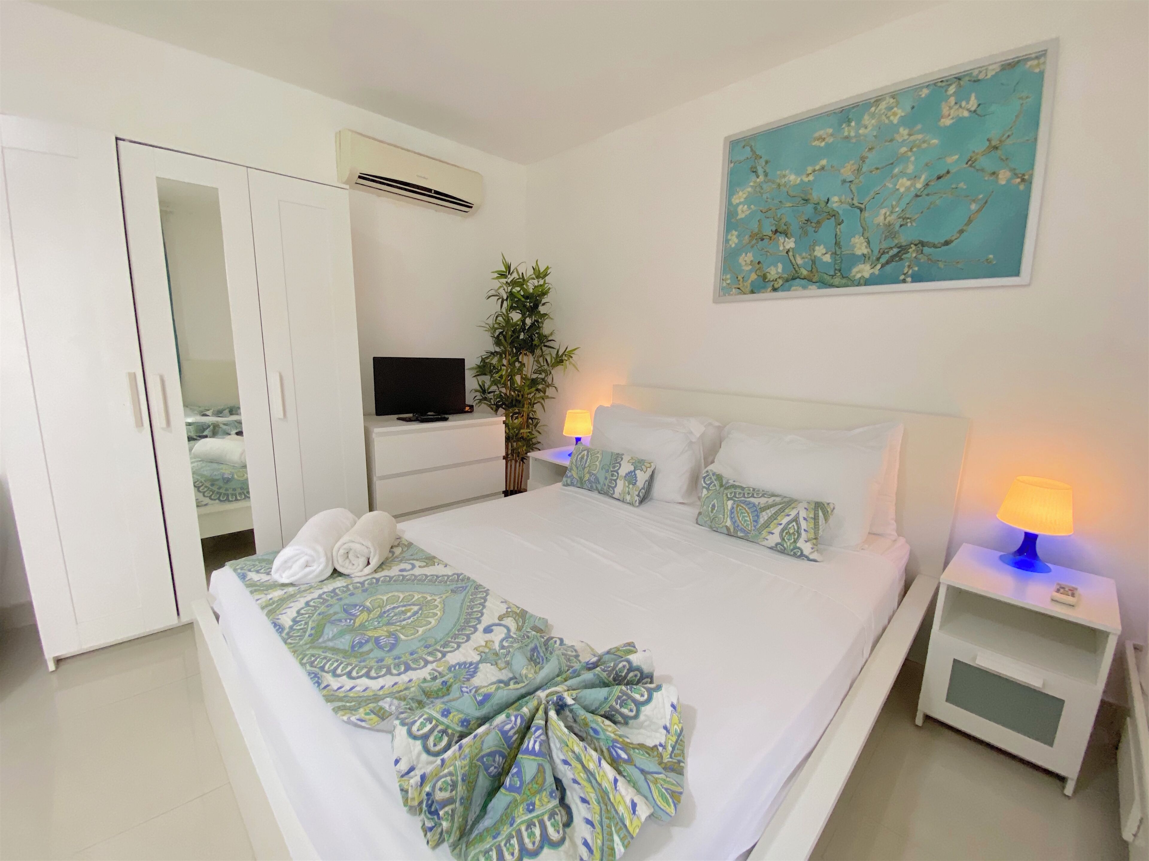 A bedroom with a bed, a TV, a plant, and a painting.