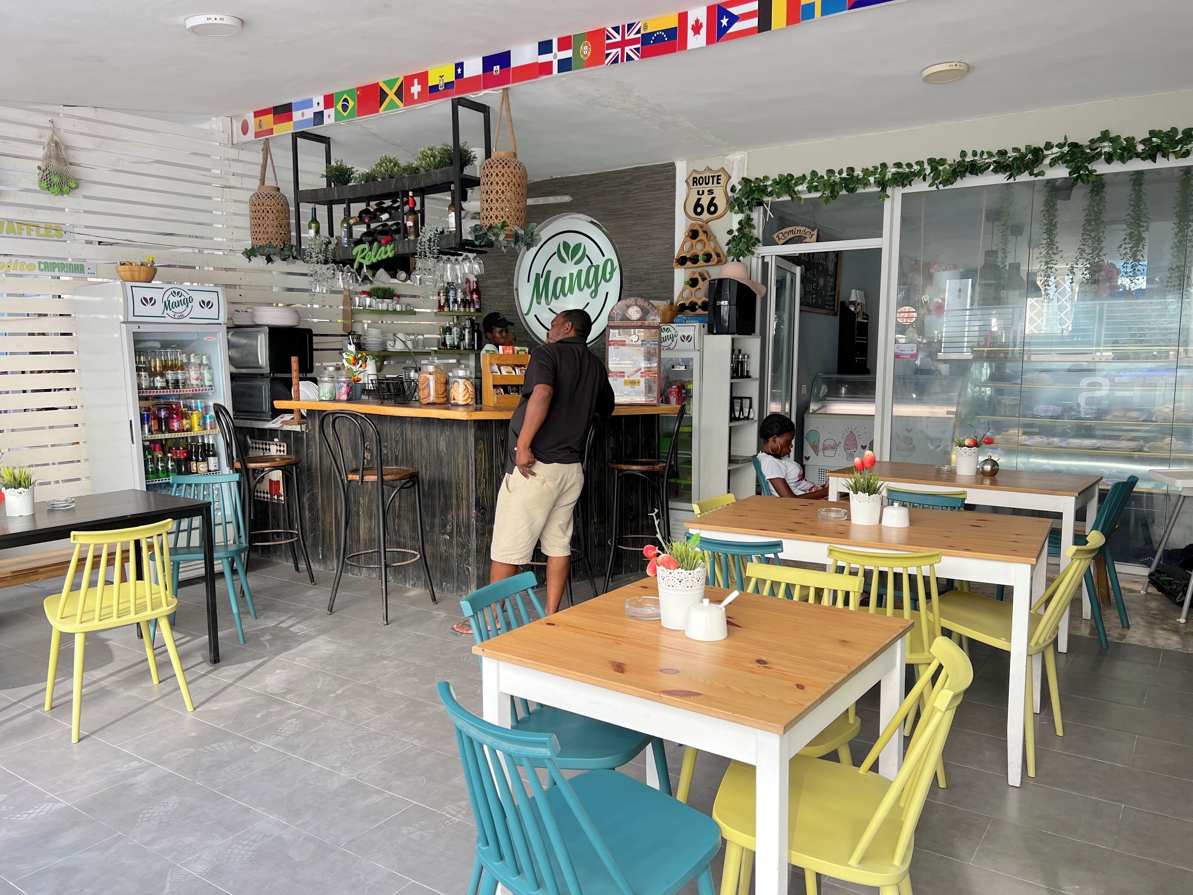 L’intérieur d’un restaurant, avec un bar, des chaises aux couleurs vives et une variété de plats et de boissons exposés.
