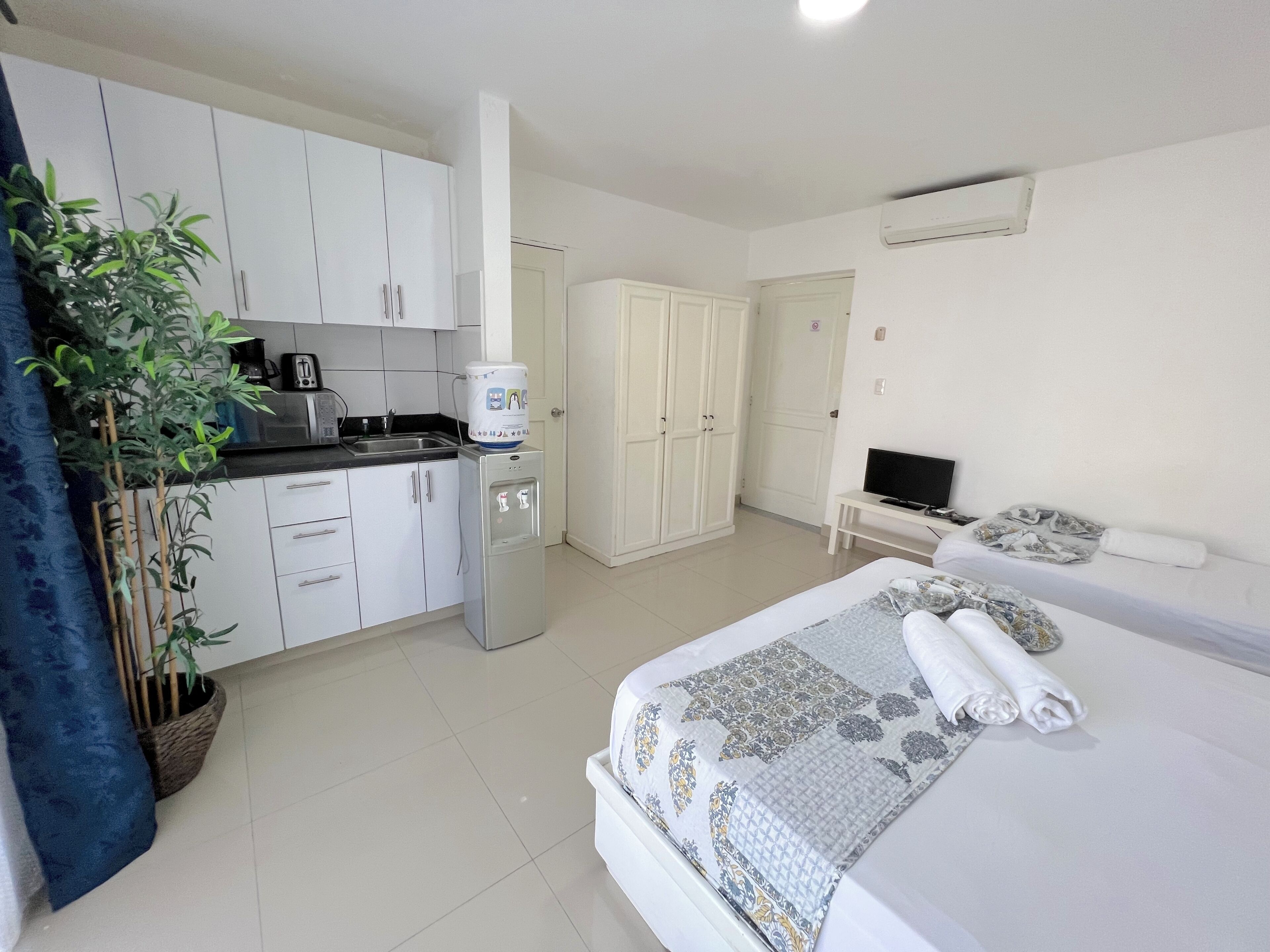 A hotel room with a bed, a TV, a small desk, and a kitchenette.