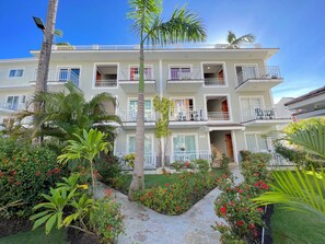 A multi-story hotel with balconies, a stone pathway, and lush greenery. - CARIBBEAN STUDIOS playa LOS CORALES (Punta Cana)