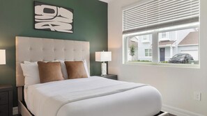 Une chambre d’hôtel avec un grand lit, une tête de lit, une table de chevet avec une lampe et une fenêtre avec des stores.