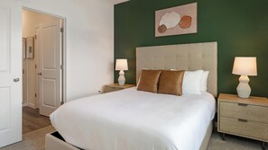 A bedroom with a large bed, two bedside tables with lamps, a green accent wall, and a door leading to another room. - Landing | Stylish 2BD, Yoga Studio, Gym (Four Corners)