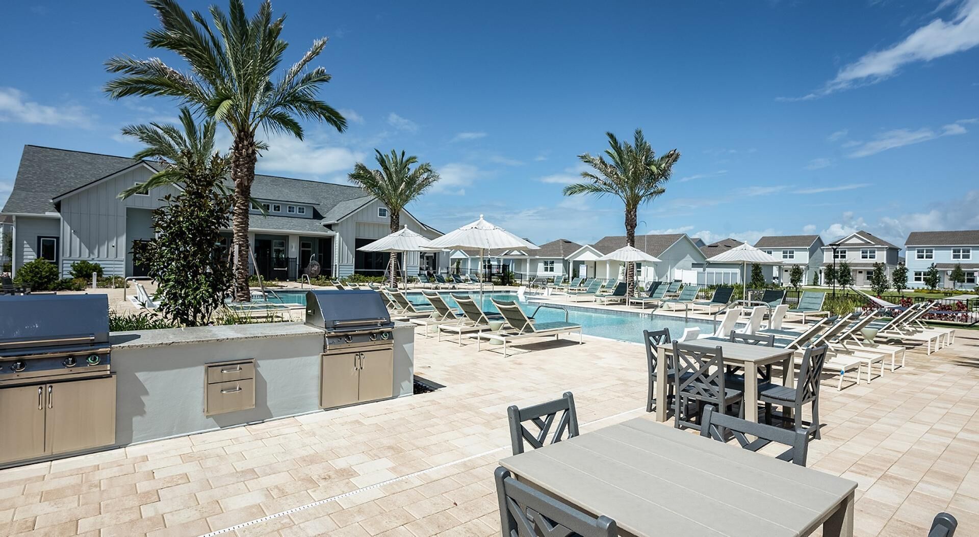 A poolside area with lounge chairs, umbrellas, and a barbecue grill.