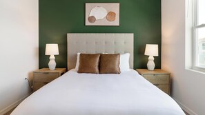 A neatly made bed with two pillows, a headboard, and bedside lamps on wooden nightstands. - Landing | Stylish 2BD, Yoga Studio, Gym (Four Corners)