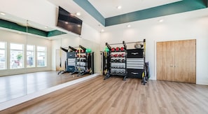 Ein Fitnessstudio mit Holzböden, Trainingsgeräten und großen Fenstern.
