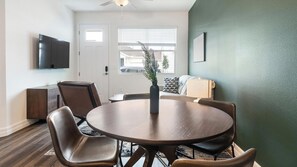 A dining area with a round table, chairs, a vase with greenery, a television on the wall, and a door with a window. - Landing | Incredible 3BD, Gym, Yoga Studio (Four Corners)