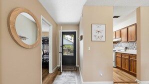 A hallway with a mirror, a door leading to a balcony, and a kitchen area with wooden cabinets. - Skiff F7 in Saint Simons Island, GA (Saint Simons Island)