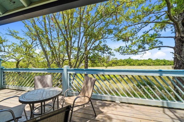 A covered outdoor seating area with a table and chairs, overlooking a natural landscape with trees and a grassy field. - Skiff F7 in Saint Simons Island, GA (Saint Simons Island)