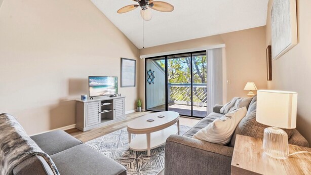 A modern living room with a sofa, a coffee table, a TV on a cabinet, and a view of the outdoors through a glass door. - Skiff F7 in Saint Simons Island, GA (Saint Simons Island)
