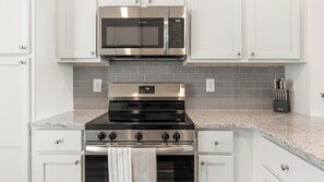 A kitchen with a stainless steel microwave, oven, and stovetop, white cabinetry, and a granite countertop. - Landing | Incredible 3BD, Gym, Yoga Studio (Four Corners)