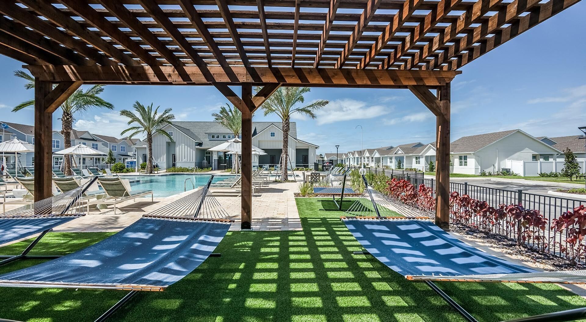 A covered outdoor area with a pool, two hammock chairs, and a view of residential buildings.