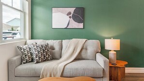 Ein Wohnzimmer mit einer Couch, Kissen, einer Decke, einer Lampe und einem gerahmten abstrakten Gemälde an der Wand.