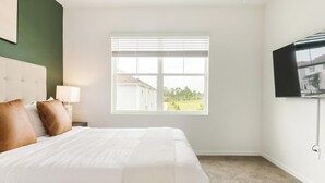 Ein Hotelzimmer mit Bett, Nachttisch, Lampe, Fernseher und einem Fenster mit Jalousien.