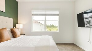 Ein Hotelzimmer mit Bett, Nachttisch, Lampe, Fernseher und einem Fenster mit Jalousien.